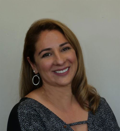 A smiling woman with dark hair, wearing a black and white top, poses for the photo.