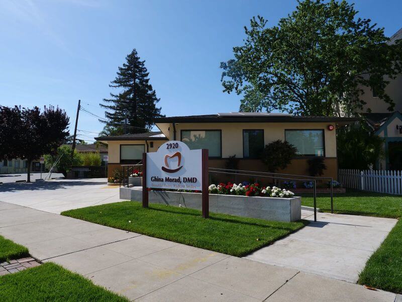 The image shows a single-story house with a sign in front that reads  1900 CHILDREN S HOSPITAL.  There is a lawn and a sidewalk, and the sky is clear.