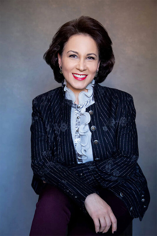 A woman in a formal suit poses for a portrait with a confident smile.