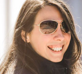 The image features a woman with sunglasses, smiling at the camera. She has short hair and is wearing a dark top.