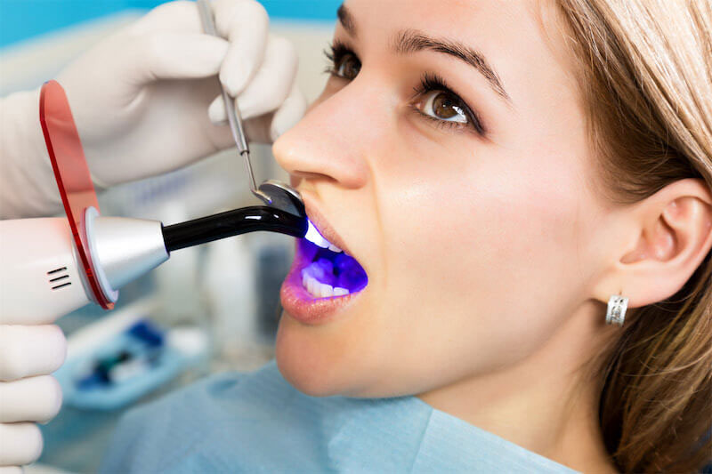 A woman in a dental chair receiving a dental implant procedure with a dentist using an implantation device.