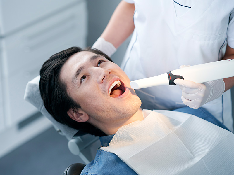The image shows a person seated in a dental chair, receiving dental treatment with a dental hygienist attending to them.