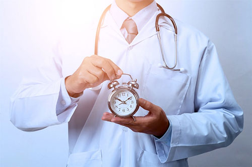 A doctor in a white coat holding a pocket watch, with the background blurred.