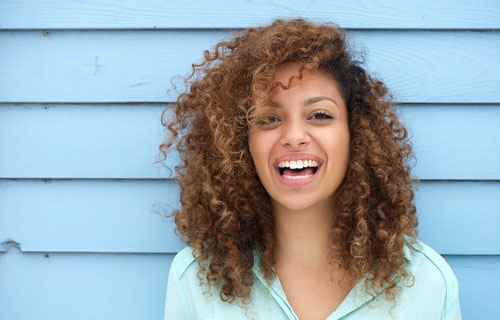 The image features a woman with curly hair and a bright smile, posing against a blue wall.