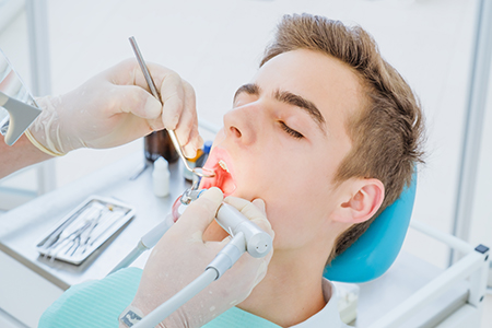 A dental professional performing a procedure on a patient s mouth, with the patient seated in a dental chair and receiving care.