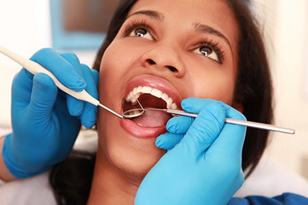 A woman in a dental chair receiving oral care, with a dentist performing a procedure using tools and wearing protective gloves.