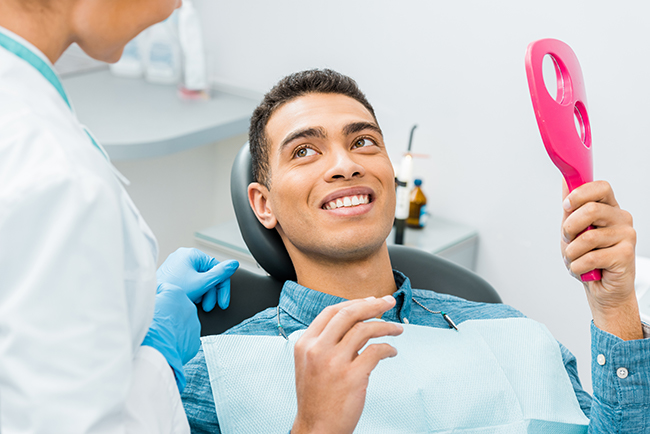 The image features a man sitting in a dental chair, holding a pink toothbrush, with a dental professional standing behind him.