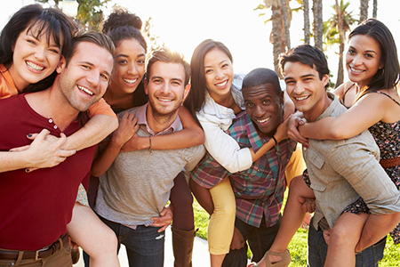 A group of young adults posing for a photo, smiling and embracing each other in a park setting.